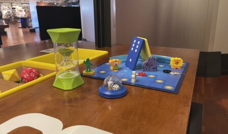Board game components (dice, hourglass, pawns) on a wooden table.