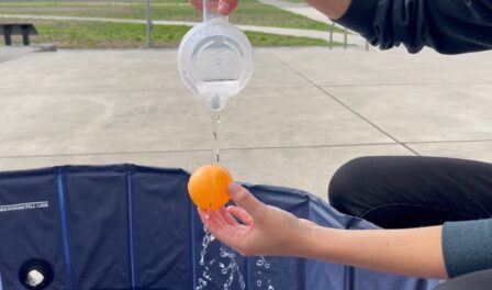 Water being poured over small orange sphere.