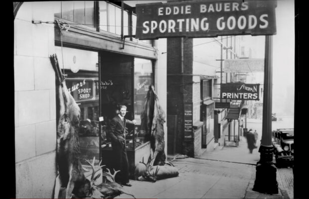 Historic black and white photo of Eddie Bauer standing outside Eddie Bauer's Sporting Goods store.
