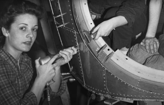 Historic black and white photo of female workers using a rivet gun to build equipment during World War II.