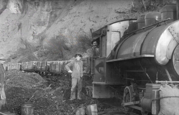 Historic black and white photo of rail workers aboard and adjacent to train in Pacific Northwest.