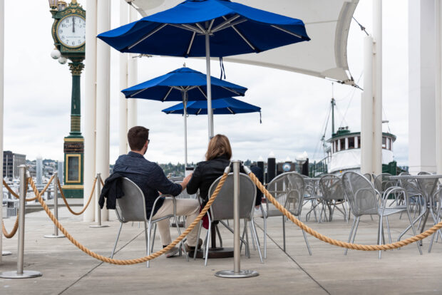 Two people sitting outside Gourmondo at MOHAI beneath a blue umbrella. The iconic Carroll's clock is to the left.