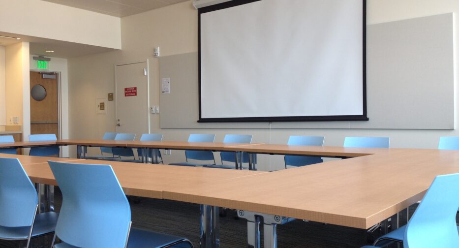 The Norcliffe conference room west shows movie screen, tables, and blue chairs.