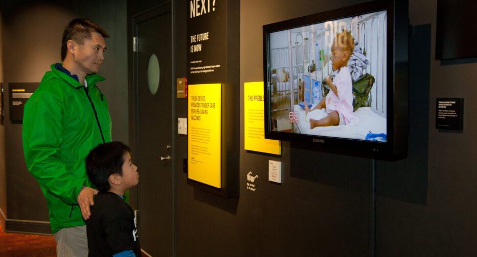 Two people looking at a screen with a baby on it next to a panel that reads, 