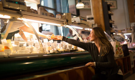 A woman reaching for cheese at the DeLaurenti cheese counter.