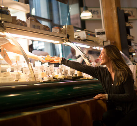 A woman reaching for cheese at the DeLaurenti cheese counter.