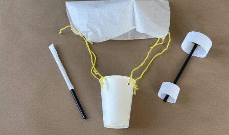 A paper cup attached to a paper parachute with yellow string.