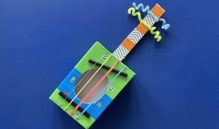 Toy guitar crafted with household supplies - rubber bands, cardboard box, colorful tape, and pipe cleaners.