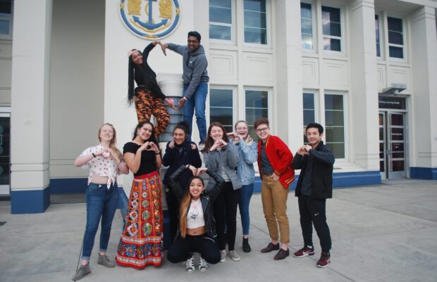 MOHAI Youth Advisors pose outside MOHAI making hearts with their hands and arms.