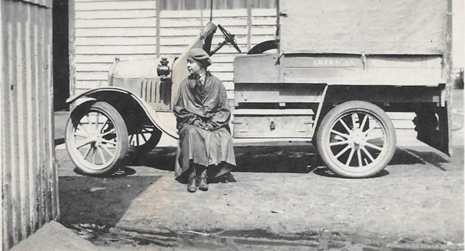 A historic black and white photo of Alice O'Brien sitting against a car.