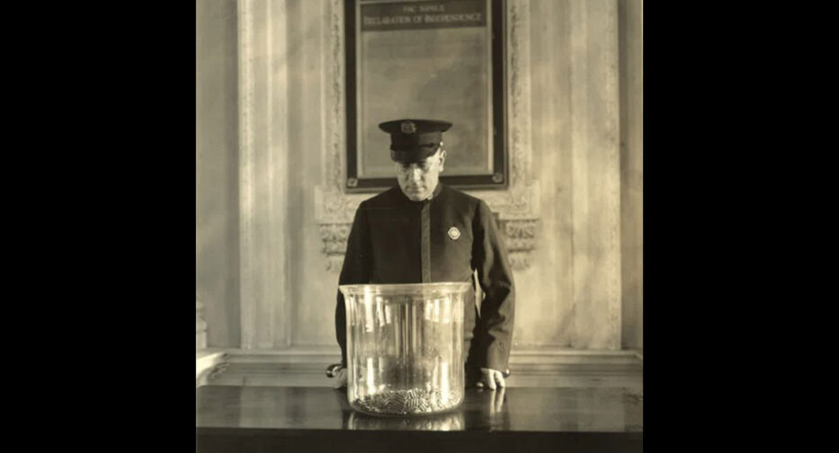Man in uniform standing in front of a large pot with balls at the bottom.