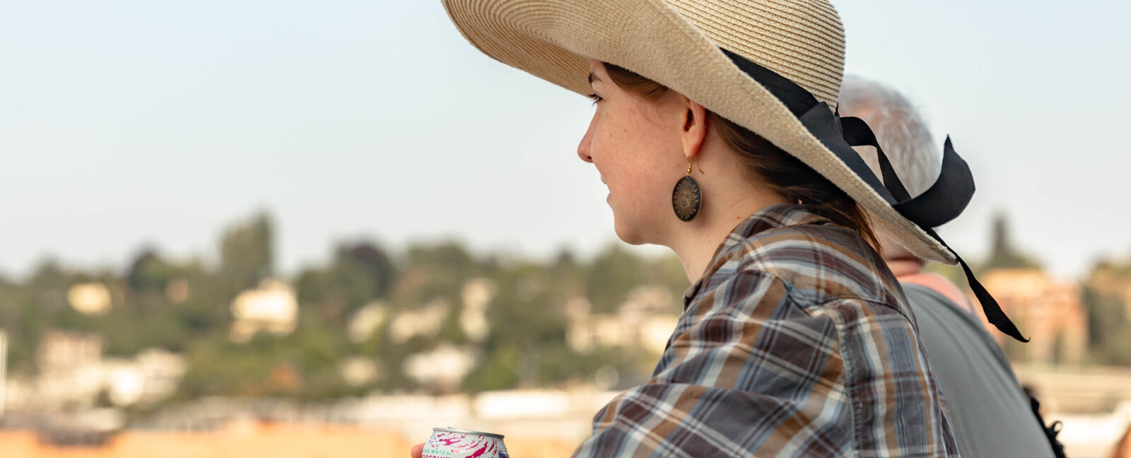 Woman wearing large sun hat drinking a grapefruit La Croix and facing to the left.
