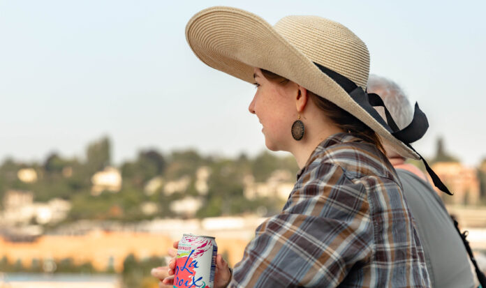 Woman wearing large sun hat drinking a grapefruit La Croix and facing to the left.