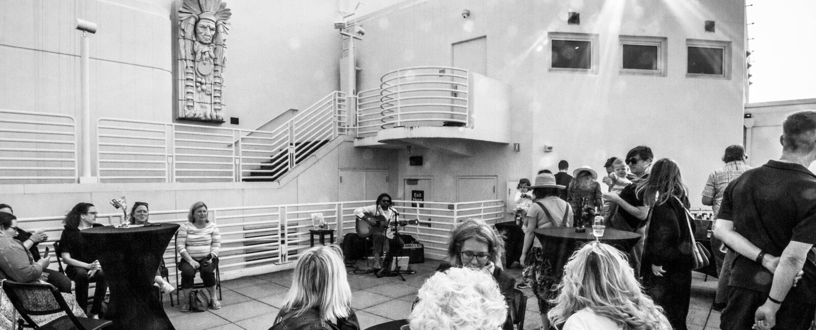 Black and white photo of Summer Nights on the Terrace attendees while Benjamin Hunter plays guitar and sing.