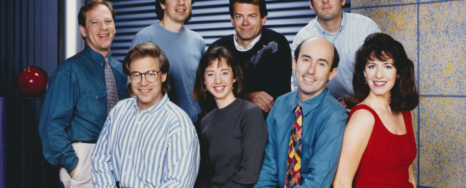 The eight member cast of Almost Live! in circa 1990s dress.
