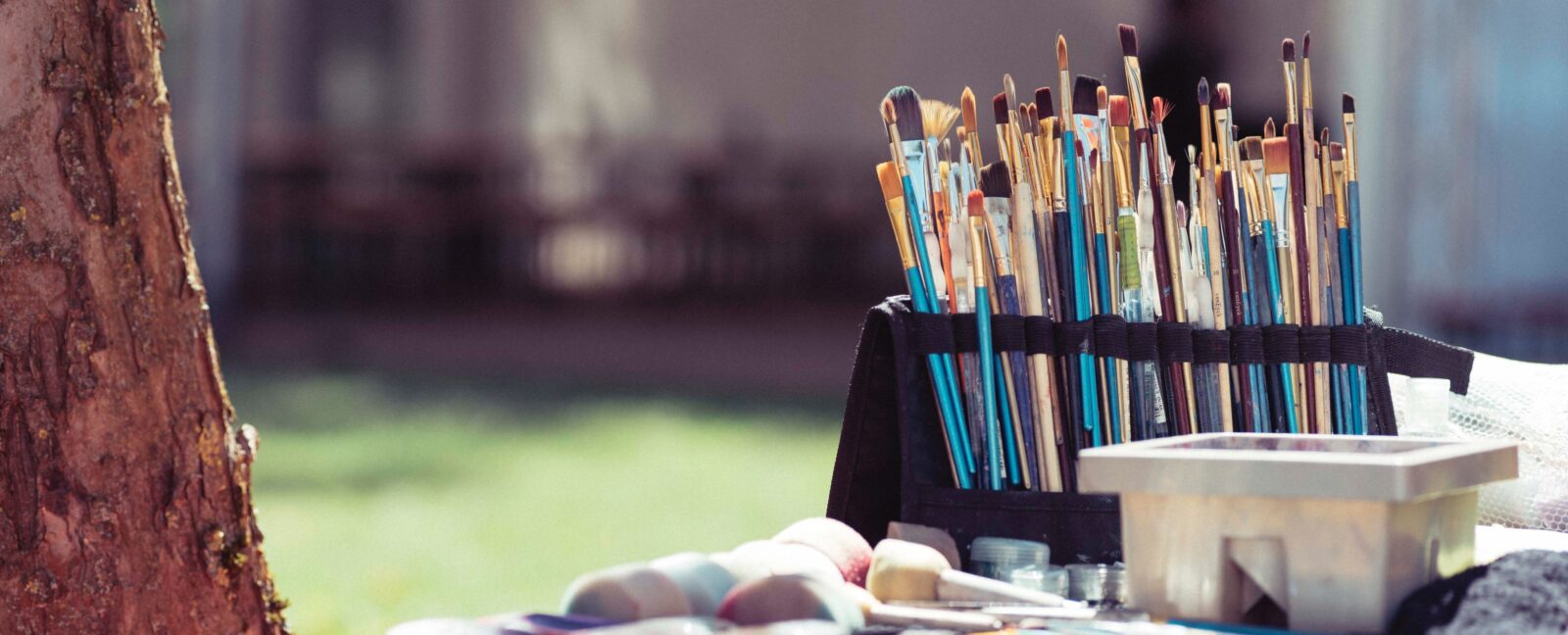 A collection of paint brushes on a table adjacent to a tree.