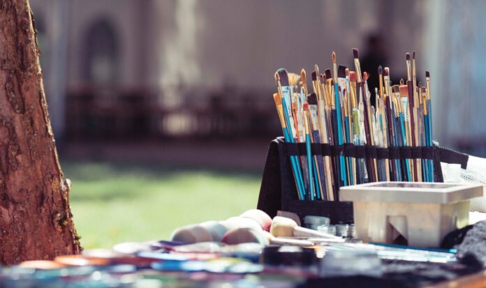 A collection of paint brushes on a table adjacent to a tree.