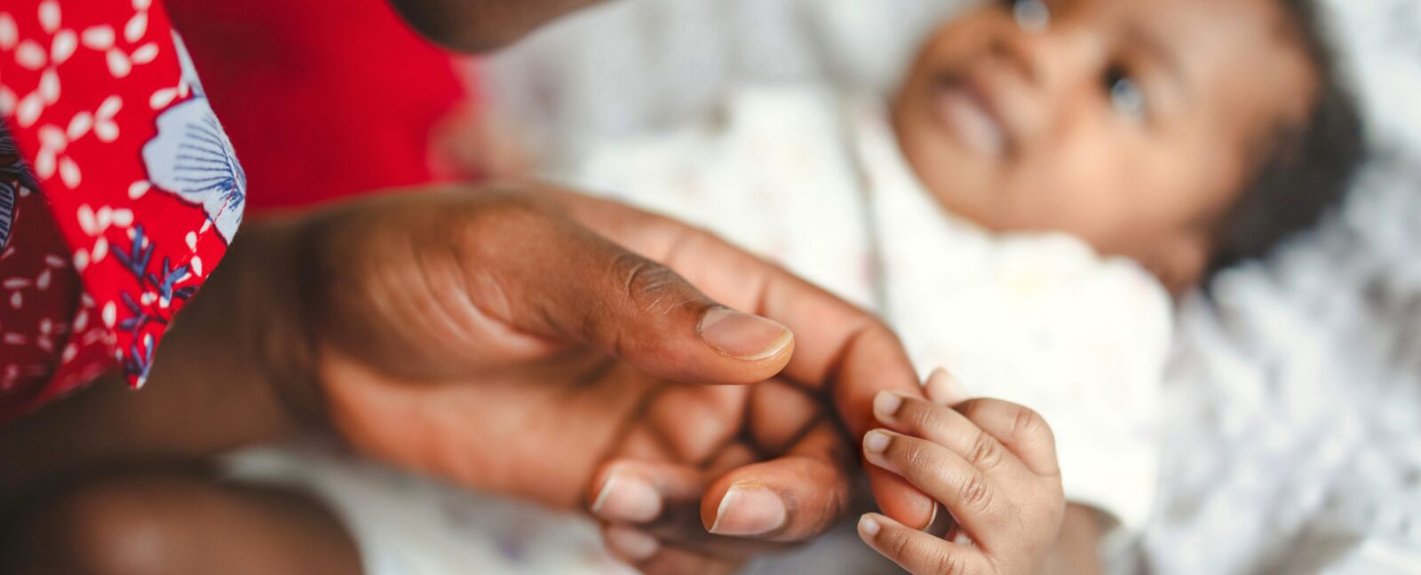A baby holds the finger of an adult.