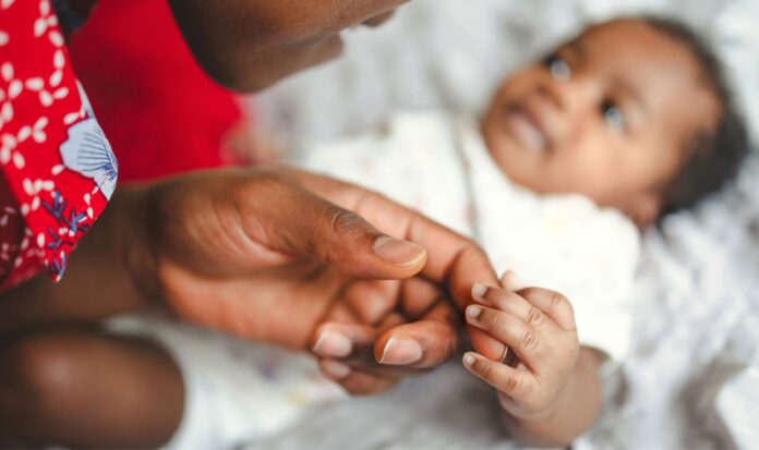 A baby holds the finger of an adult.
