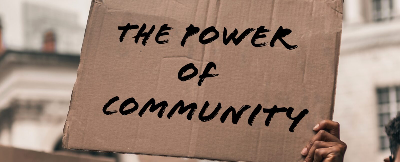 A single hand holding a cardboard sign that reads
