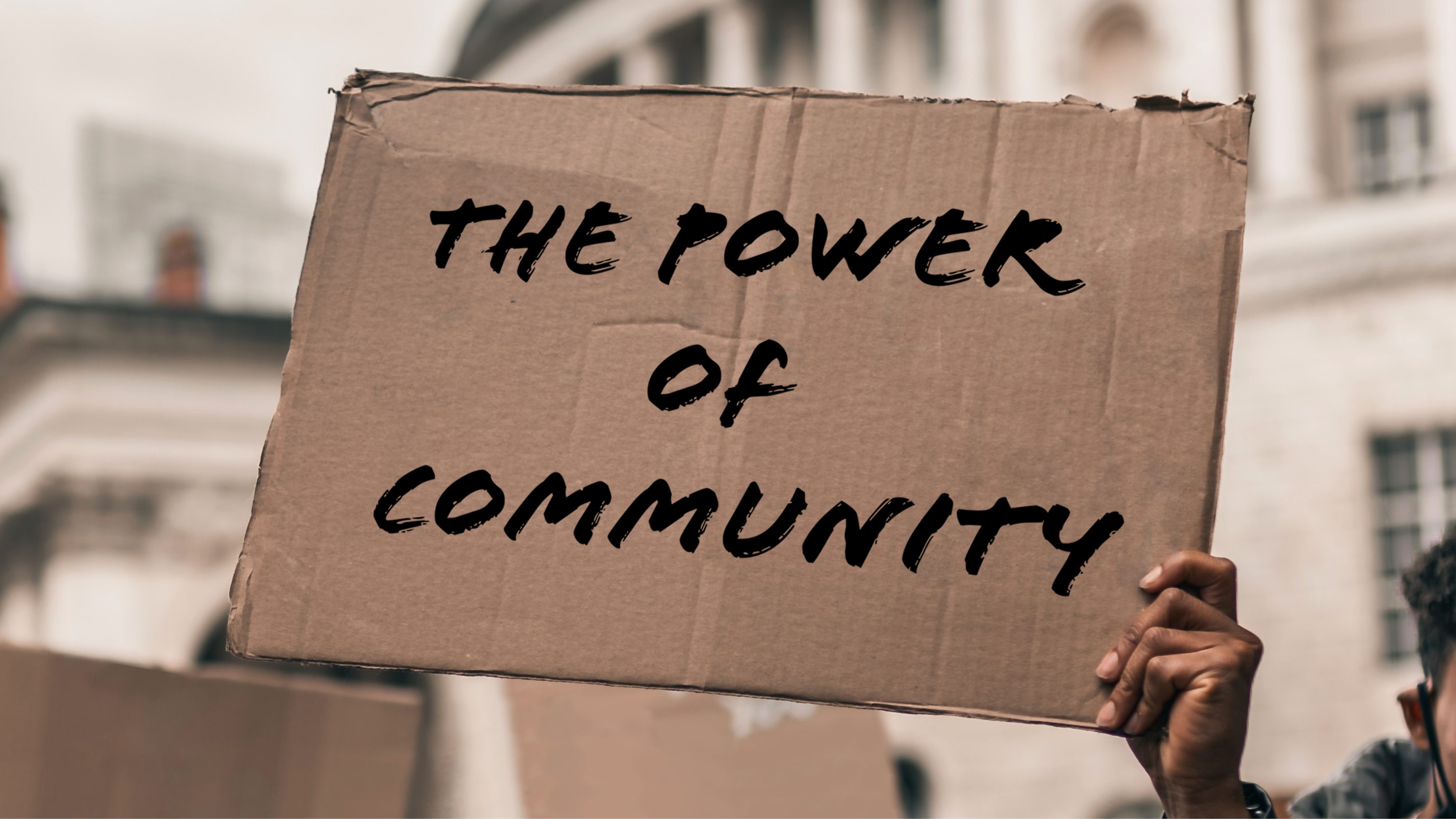 A single hand holding a cardboard sign that reads