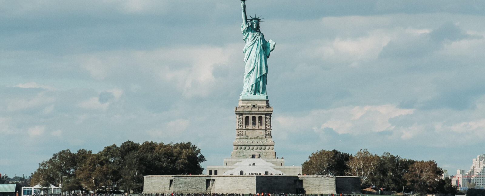 The Statue of Liberty stands against a cloudy sky.