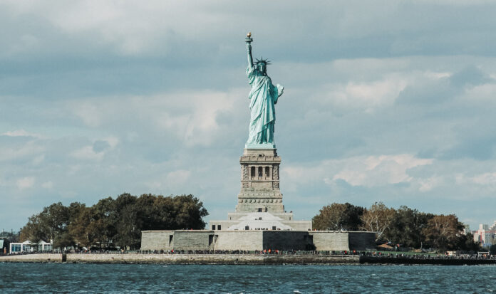 The Statue of Liberty stands against a cloudy sky.