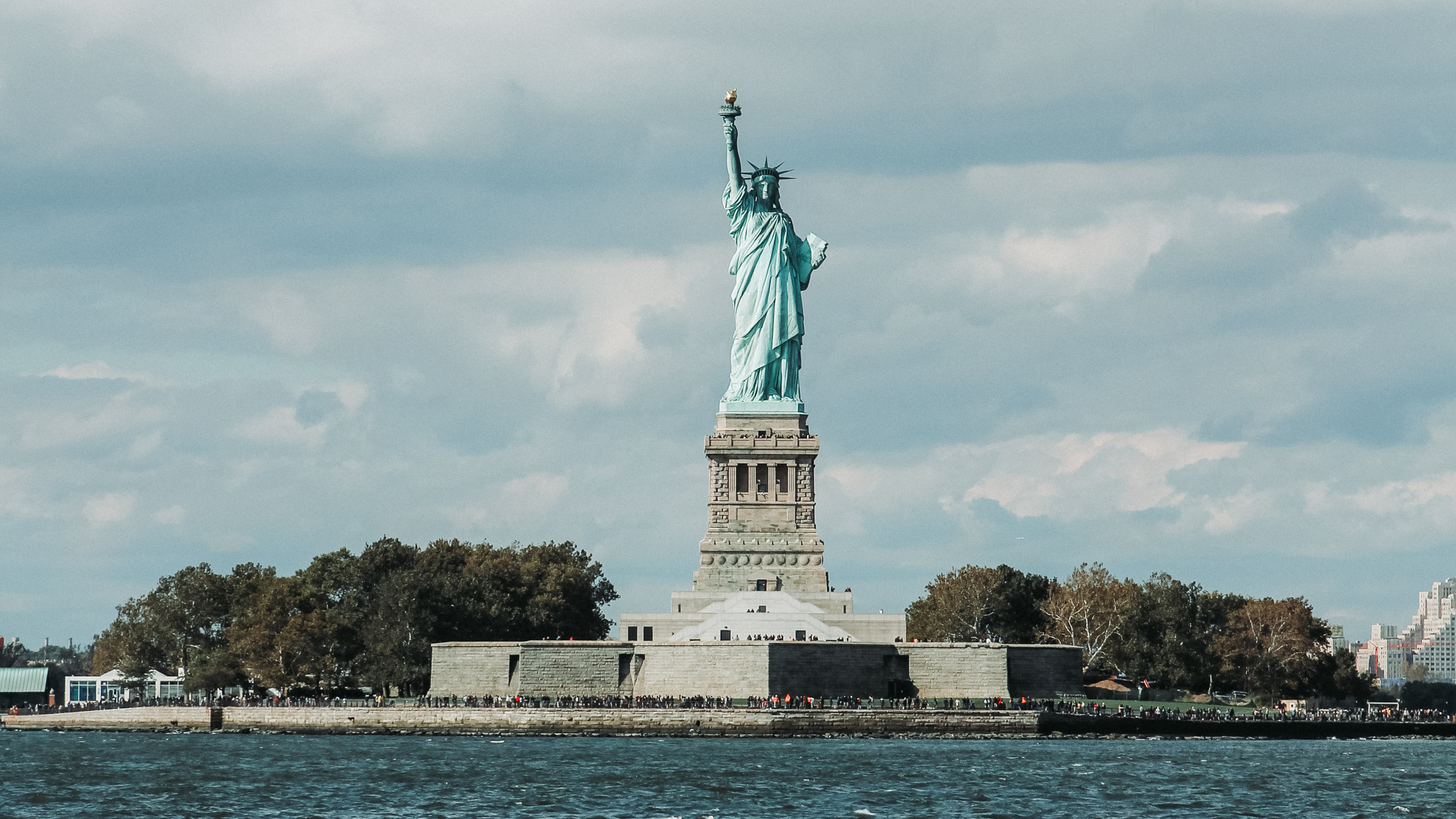The Statue of Liberty stands against a cloudy sky.