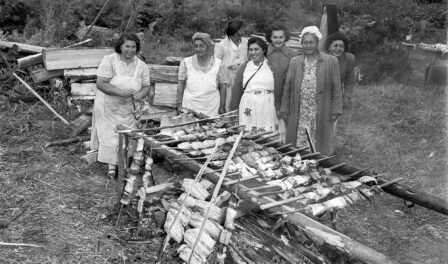 Seven women cooking salmon over a wood fire, Muckleshoot Reservation, circa 1950.