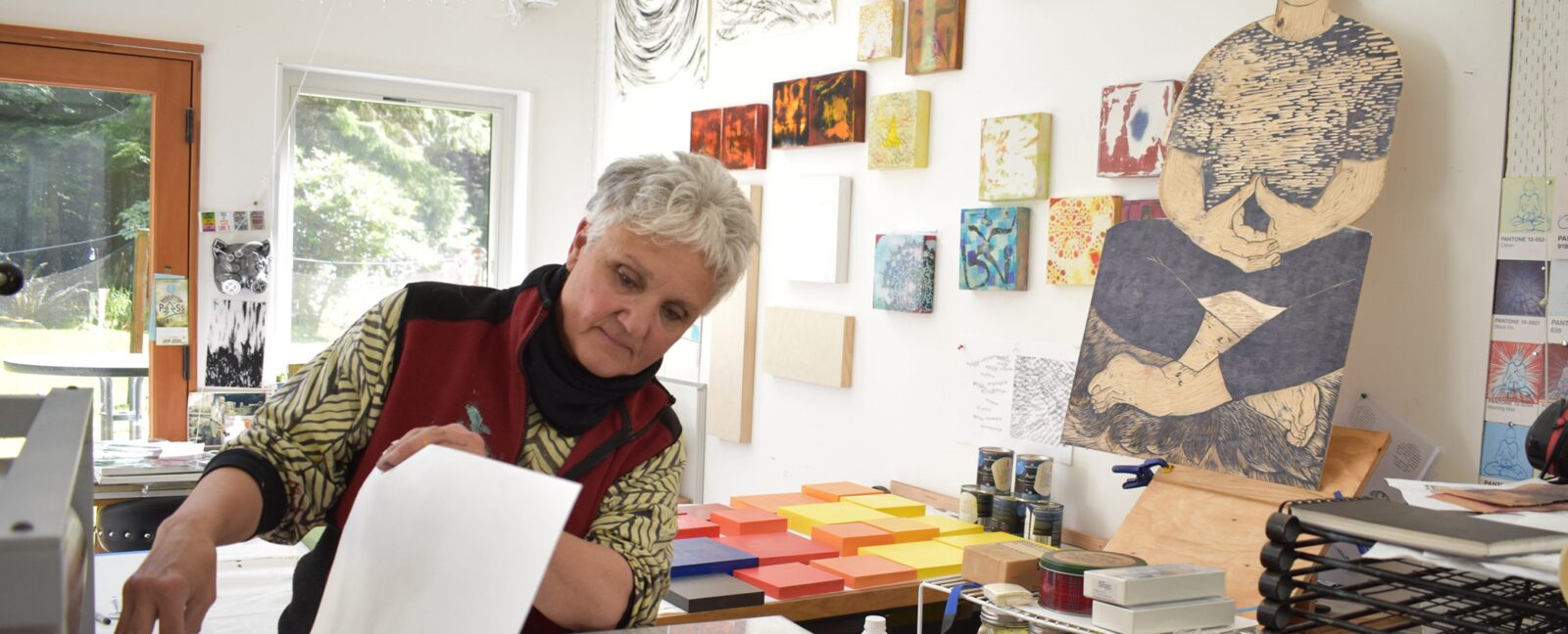 Person with white hair exploring printing in a room with white walls and hanging art.