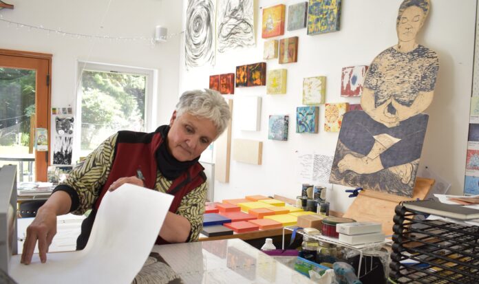 Person with white hair exploring printing in a room with white walls and hanging art.