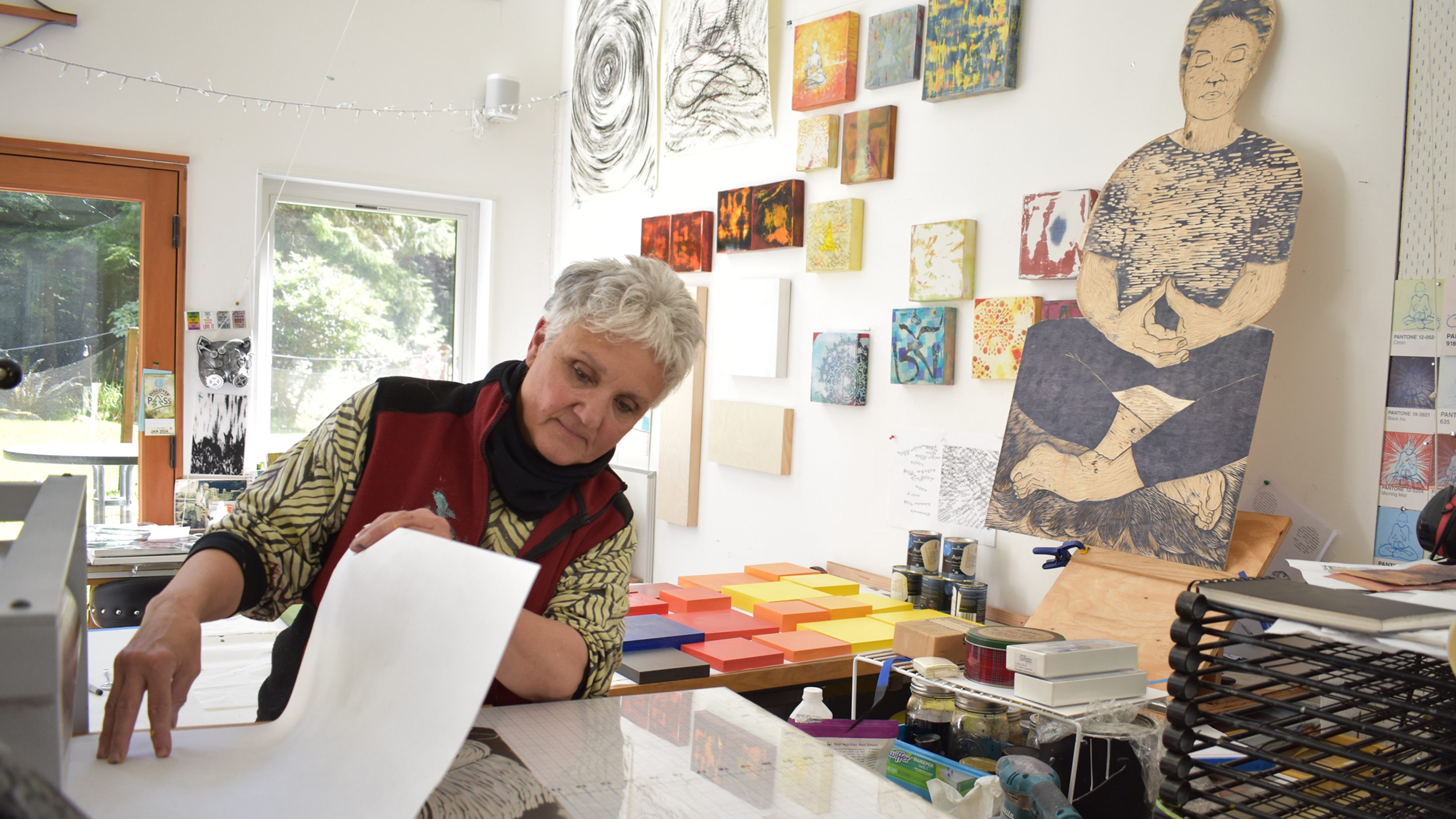 Person with white hair exploring printing in a room with white walls and hanging art.