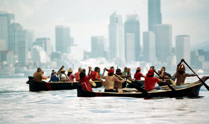 Two groups of indigenous peoples row two canoes across the Puget Sound near Seattle