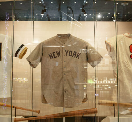 Five historic Major League Baseball uniforms behind glass. Visible teams include Dodgers, Yankees, and Giants.