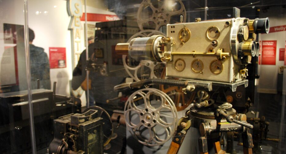 An antique movie projector supported by a wooden tripod on display at MOHAI.