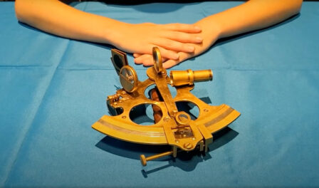 A sextant, golden in color, sits on a blue table.