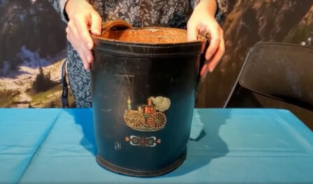 An antique leather fire bucket displayed on a blue table.