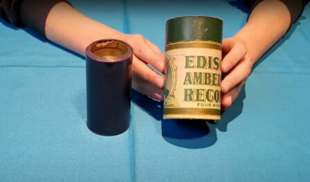 An antique cylinder record displayed on a blue table.