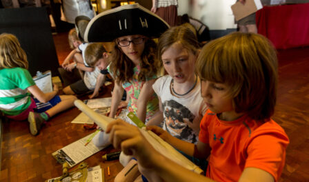 Children working together on a field trip to MOHAI. One child wears a large pirate hat.