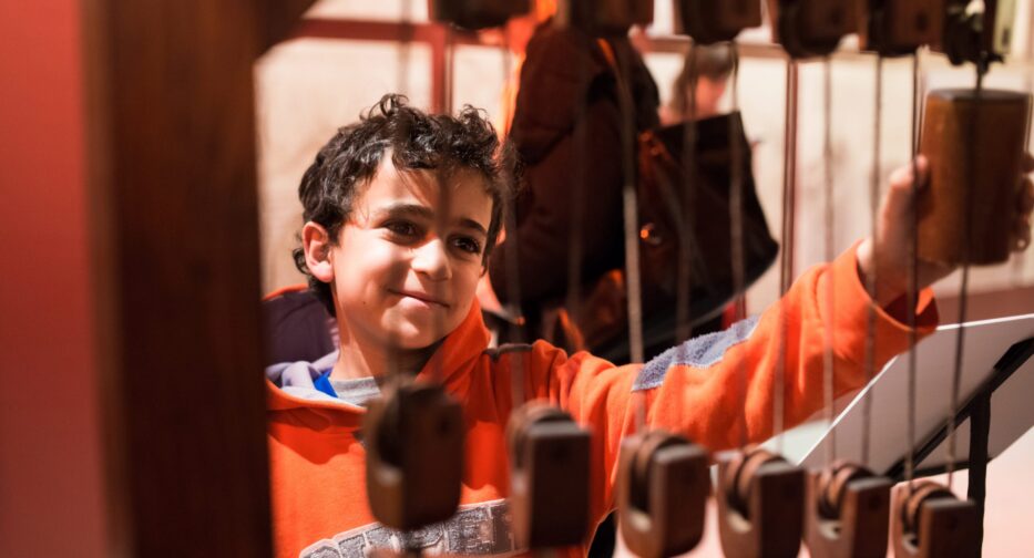 Young person in orange hooded sweatshirt interacting with pulley system at Leonardo da Vinci - Inventions Exhibit.