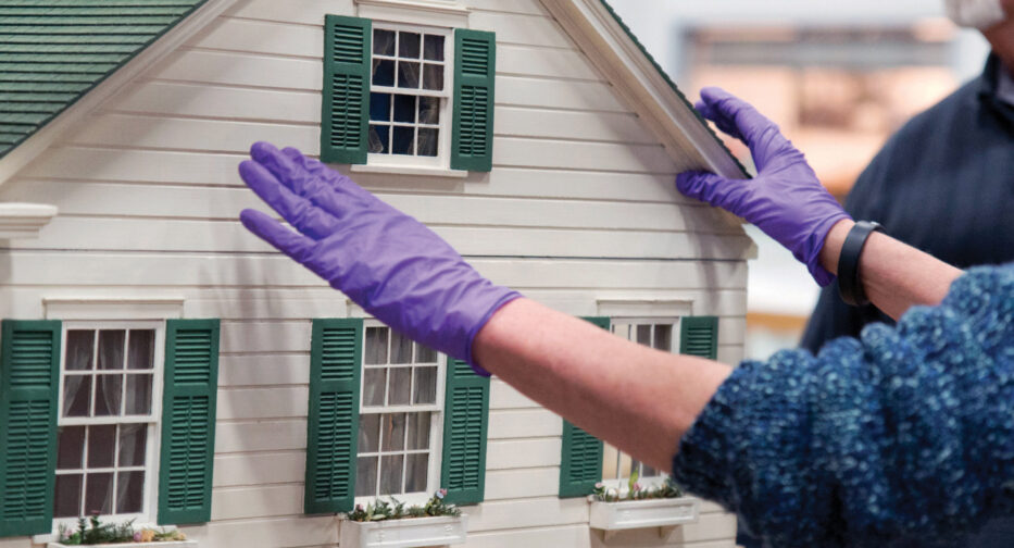 A MOHAI employee wearing purple gloves sets up the Hammons House.