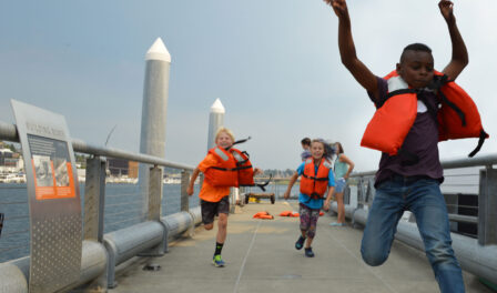 Children wearing orange life preservers and running on a Lake Union dock in downtown Seattle, WA.