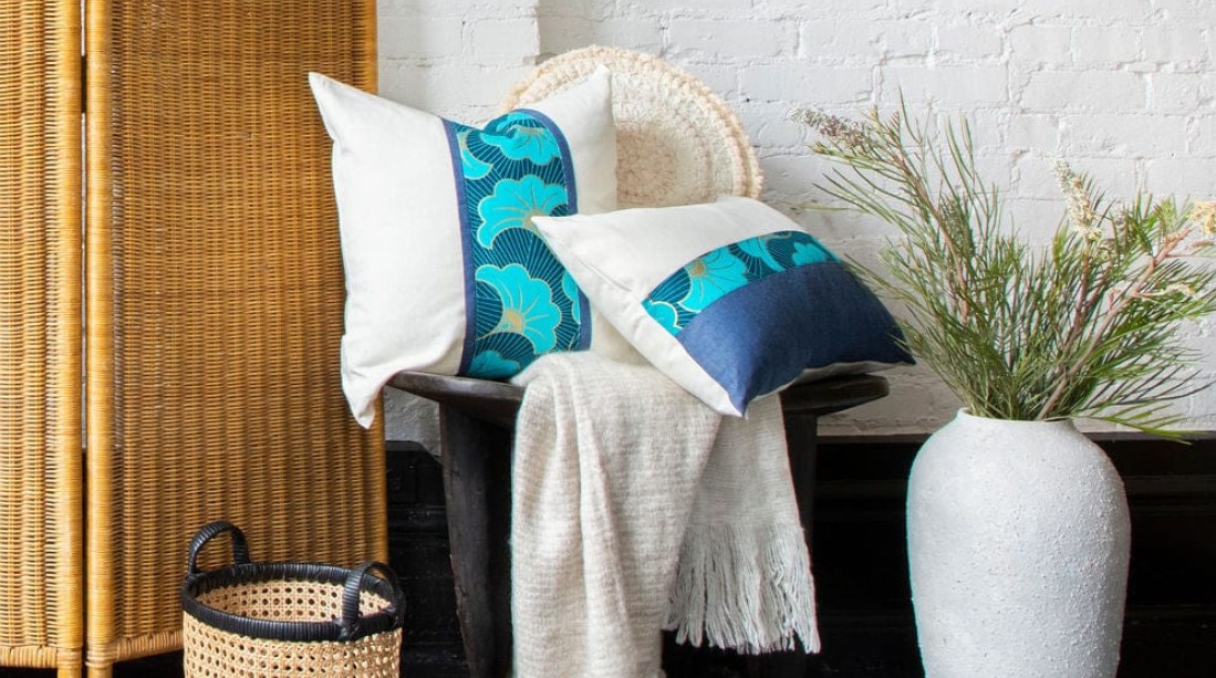 White and blue pillows on a wooden chair adjacent to a wicker privacy screen.