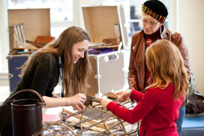 A MOHAI employee works with a student to weave branches during a field trip activity.