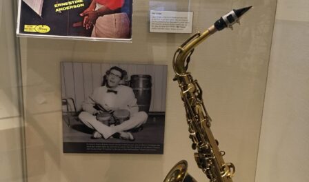 An alto saxophone and bongos adjacent to a photo of Norm Bobrow on display at MOHAI.