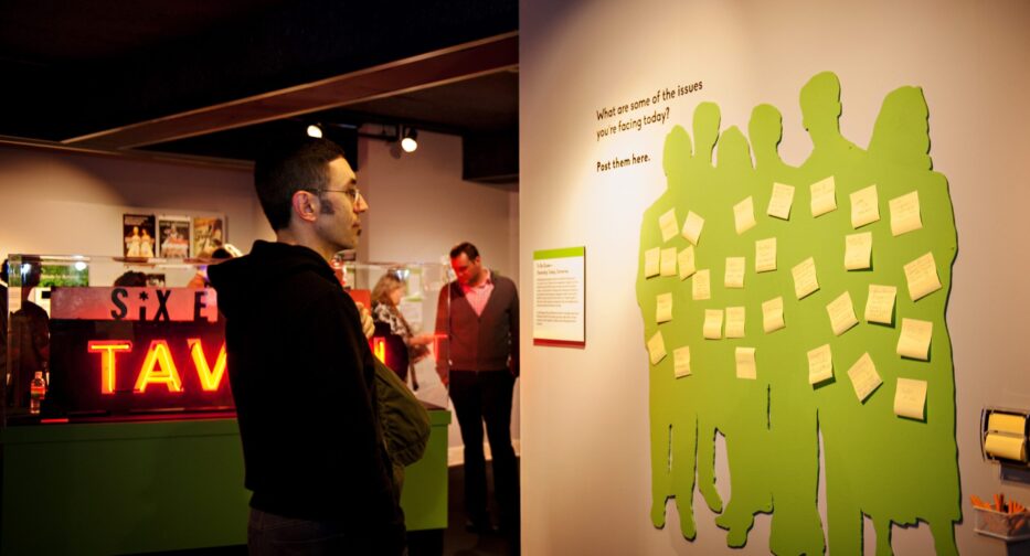 Person facing to the right looking at green paper cutout of a group of six people with yellow sticky notes on them.