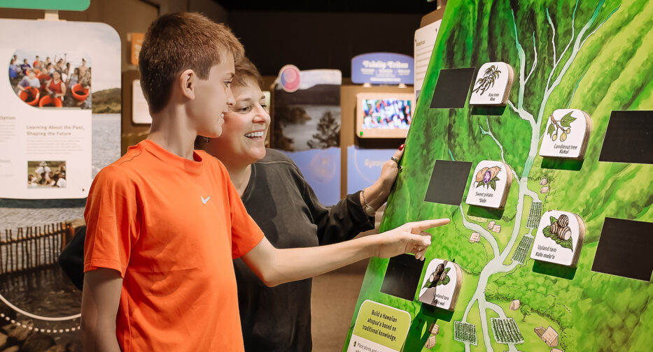 Two people standing to the let of a green activity board.
