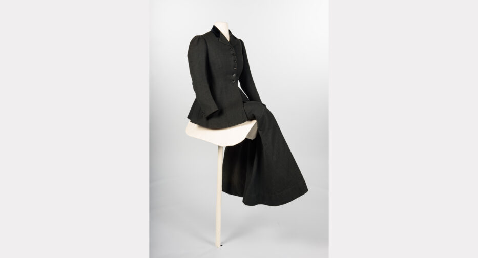 A black sidesaddle riding habit (Shogren, ca. 1907) featuring a tailored skirt that fits tightly around the legs. The hem appears asymmetrical when standing, but when the wearer is mounted sidesaddle, it hangs straight.