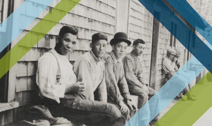 Migrant laborers sitting against side of home covered with cedar shakes.