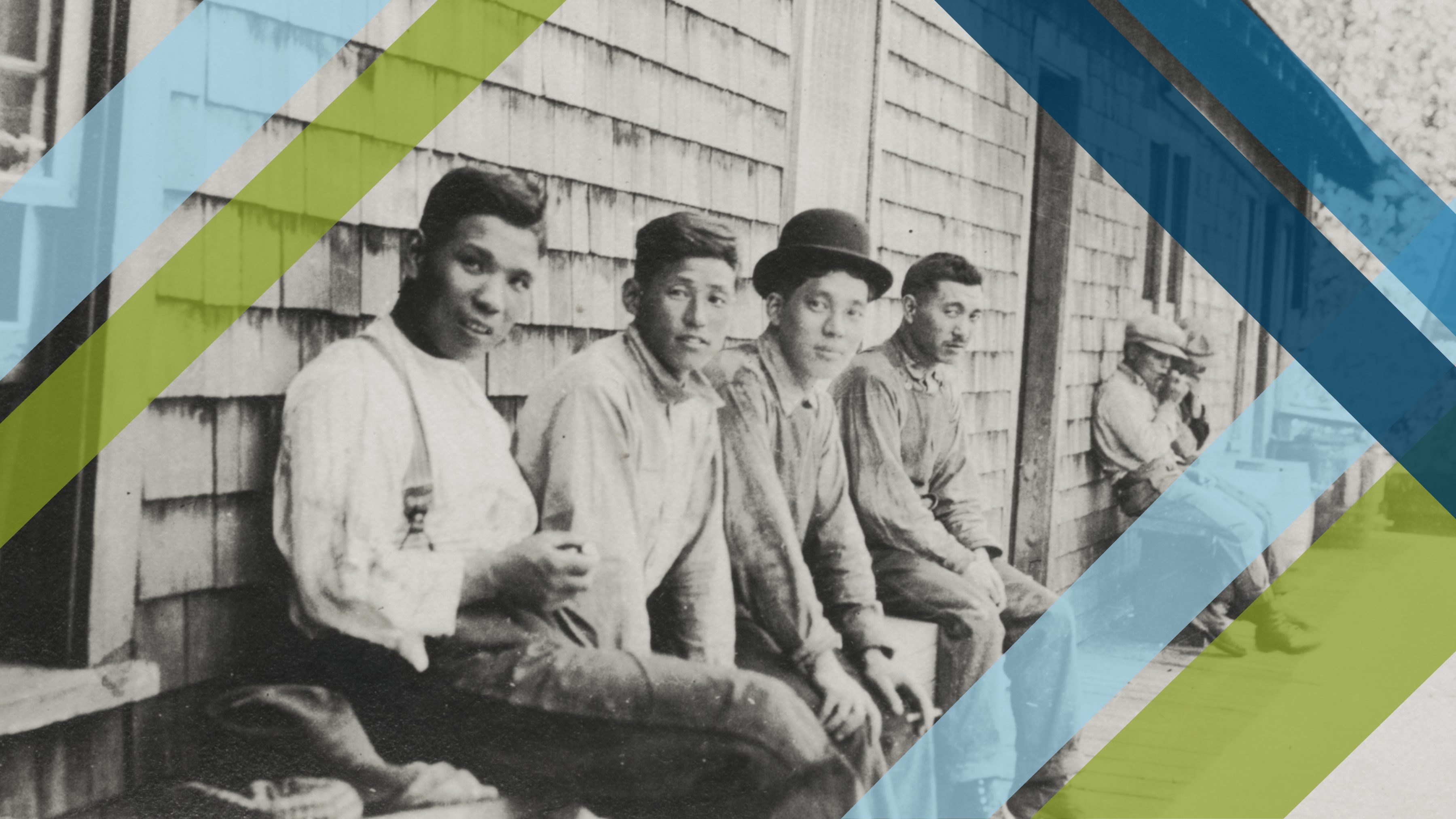 Migrant laborers sitting against side of home covered with cedar shakes.